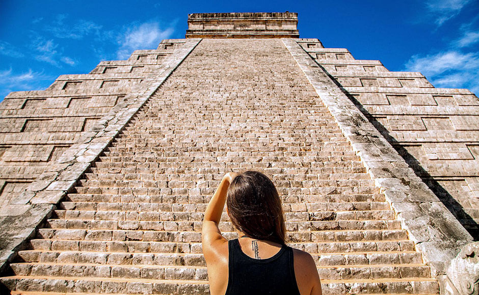 Woman standing in front of Chichen Itza pyramid stairs looking up to the top
